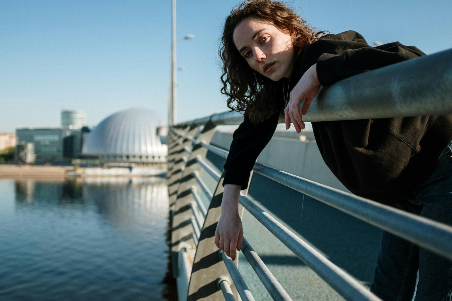 Woman in Black Long Sleeve Shirt and Black Pants Sitting on White Wooden Bridge