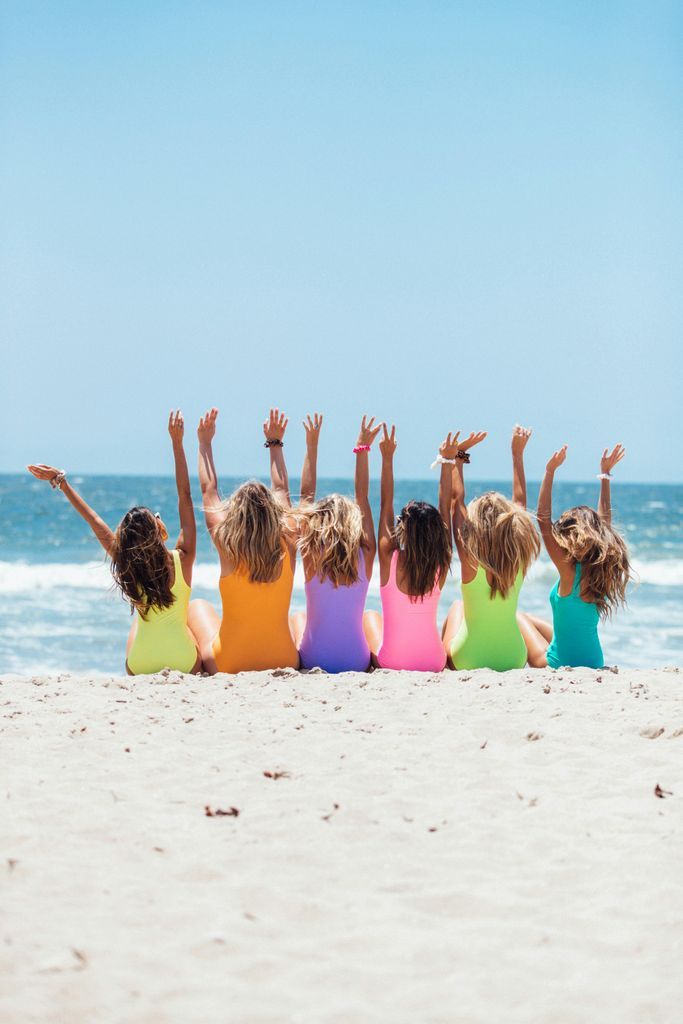 Back view photo of six girls wearing swimsuit sitting on white sand