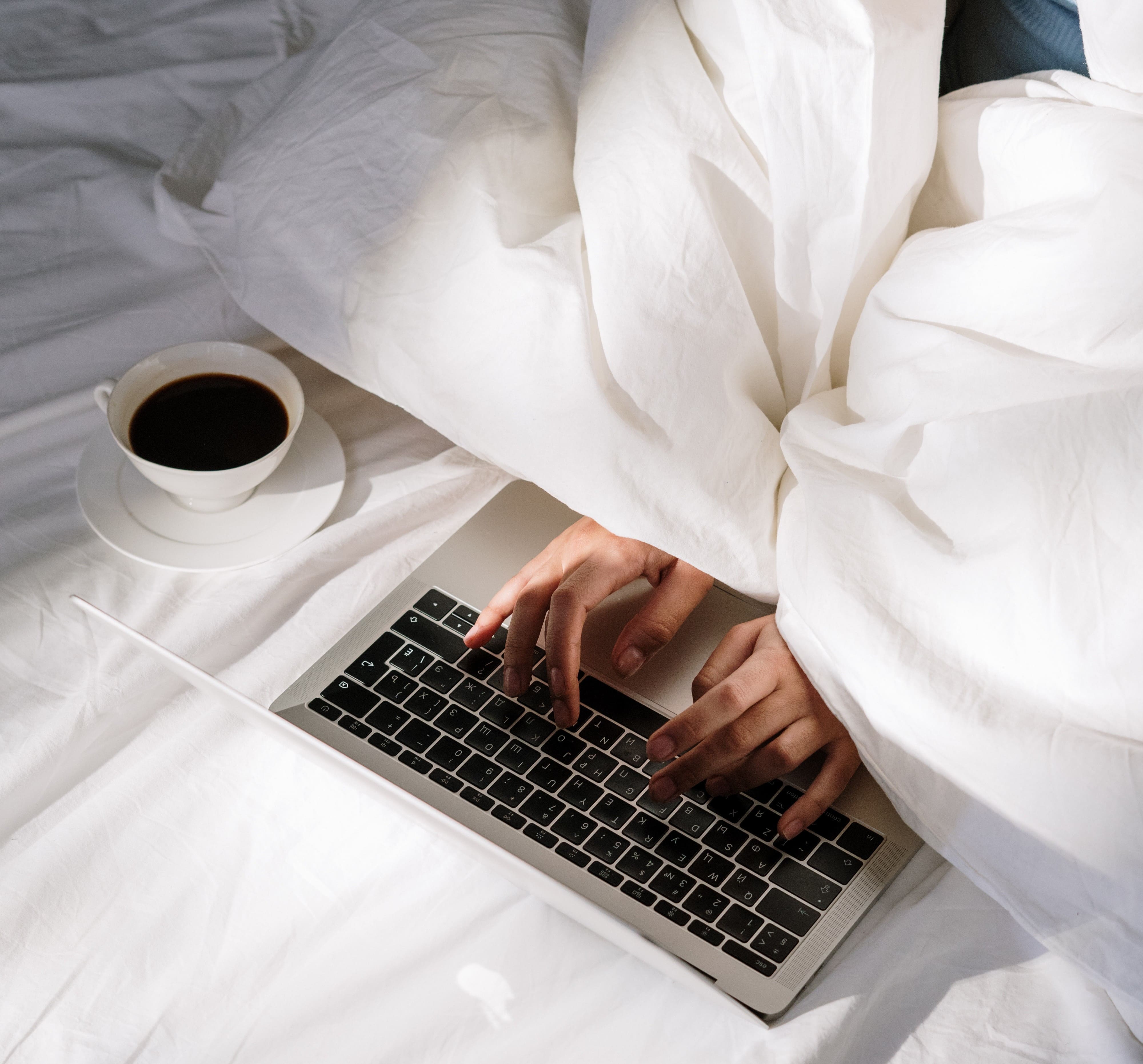 working from bed under the blanket with a coffee cup on the mattress